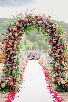 an outdoor ceremony with flowers and greenery on the aisle, along with wooden benches