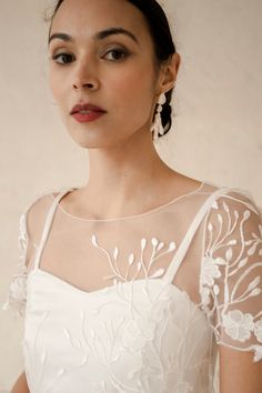 a woman in a white dress with an intricate design on her shoulder and neckline