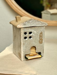 a birdhouse made out of concrete sitting on top of a white table cloth next to a mirror