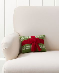 a white chair with a green and red christmas pillow on it's back, sitting in front of a white wall