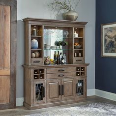 a dining room hutch with glass doors and shelves on the top shelf, in front of a blue wall