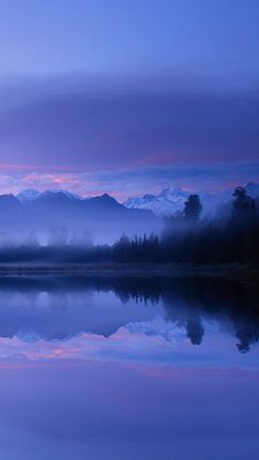 a lake with mountains in the background and fog hanging over it's surface at dusk