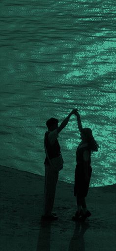 two people standing on the beach with their hands in each others's heart shape