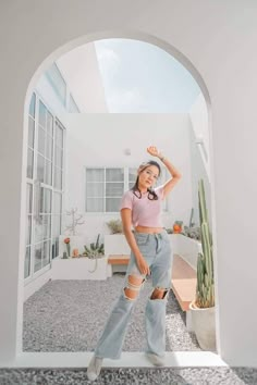 a woman standing in front of an arch wearing ripped jeans and a pink t - shirt