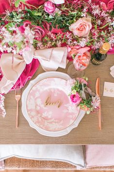 the table is set with pink flowers and white plates, silverware, and napkins