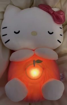 a hello kitty stuffed animal sitting on top of a bed next to a lit candle