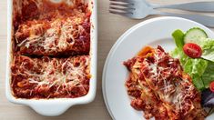 a white plate topped with lasagna next to a bowl of salad and fork