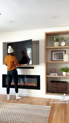 a woman standing in front of a fireplace with a tv on it's wall