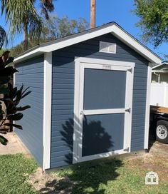 a small gray shed sitting on top of a grass covered field next to a palm tree