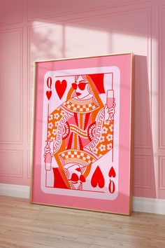 a pink and gold framed playing card on a wooden floor in front of a pink wall