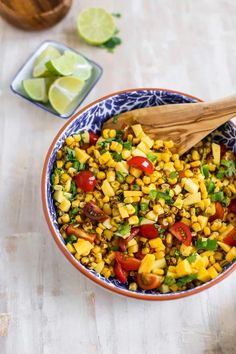 a bowl filled with corn and vegetables on top of a table next to limes