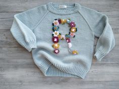 a blue sweater with flowers on it and the letter q is made out of yarn