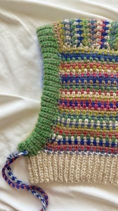 a crocheted bag is laying on a white sheet with blue, green, and red yarn