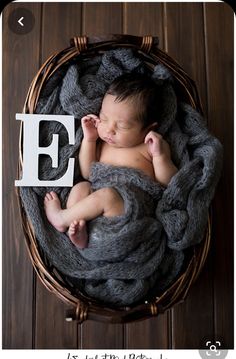 a newborn baby is curled up in a basket with the letter e on it's side