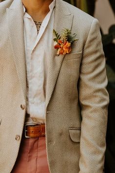 a man wearing a tan suit and orange flower boutonniere with his hand in his pocket