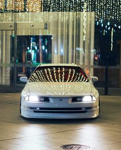 a white car parked in front of a tall building with lights on it's windows