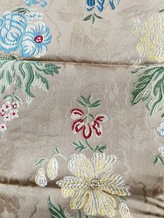 close up view of an embroidered fabric with flowers and leaves on the side, in neutral colors