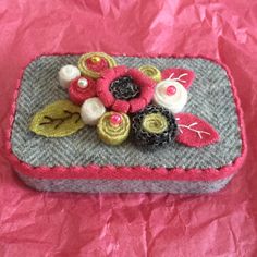 a small purse with flowers on it sitting on a pink cloth covered tablecloth,