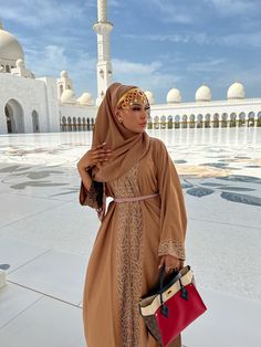 a woman standing in front of a white building with a red handbag on her hip