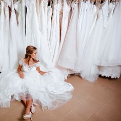 a woman sitting on the floor in front of wedding dresses