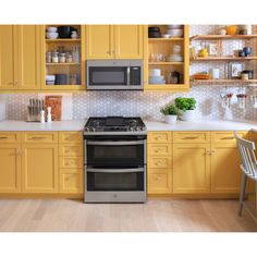 a kitchen with yellow cupboards and stainless steel stove top oven in the middle of it