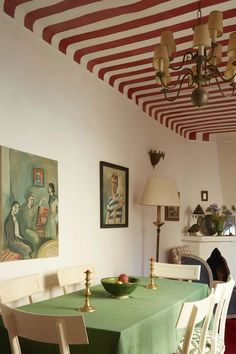 a dining room with a green table cloth and white chairs in front of a painting on the wall