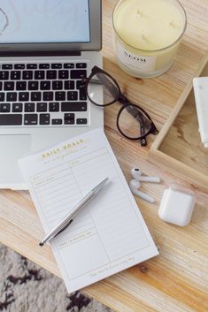 an open laptop computer sitting on top of a wooden desk next to a pen and glasses