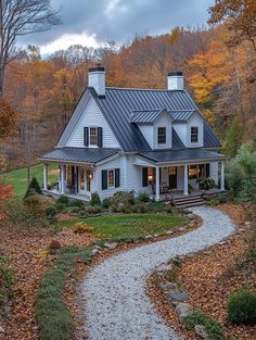 a white house in the fall with leaves on the ground and trees around it,