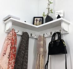 three scarves and a purse hanging on a white coat rack with two hooks, one holding a black purse