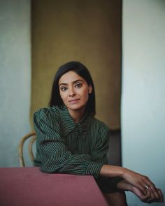 a woman sitting at a table with her hand on her shoulder and looking off to the side