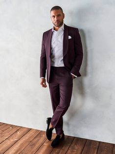 a man in a purple suit leaning against a wall with his hands in his pockets