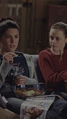 two women sitting on a couch eating food and drinking beverages in front of each other