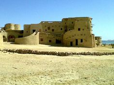 an old building sitting in the middle of a desert area with water in the background