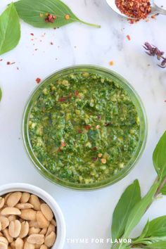 a bowl filled with green pesto next to two small bowls full of peanuts and leaves