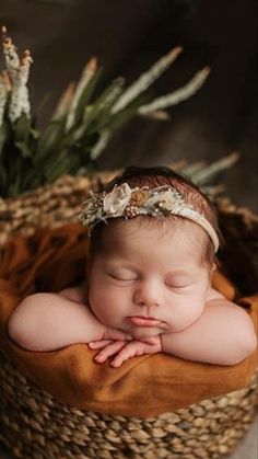 a baby is sleeping in a basket with flowers on it's head and hands