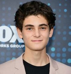 a young man in a suit and black shirt smiling for the camera at an event