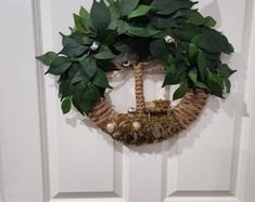 a wreath hanging on the front door with green leaves and other things around it,