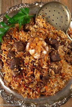 a silver bowl filled with rice and meat on top of a wooden table next to a metal strainer