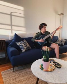 a person sitting on a couch with a guitar in their hand and a potted plant next to it