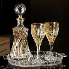 two wine glasses and a decanter sitting on a glass tray in front of a black background