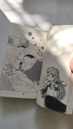 a hand holding an open comic book with drawings on the pages and in front of it