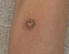 a small heart tattoo on the ankle with sunbursts in the middle and behind it