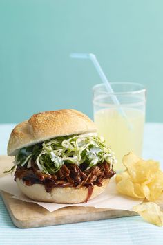 a pulled pork sandwich with cole slaw on a cutting board next to a glass of lemonade