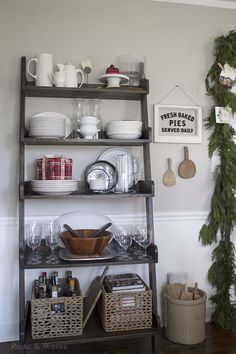 a shelf filled with dishes and cups on top of a wooden floor next to a christmas tree