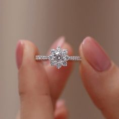 a close up of a person holding a ring with a flower shaped diamond on it