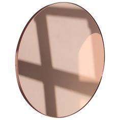 a round mirror reflecting the shadow of a cross on it's side, in front of a white wall