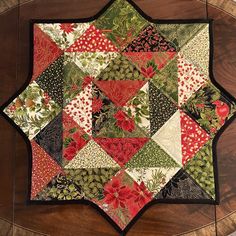 a quilted table topper with red, green and white flowers on the center