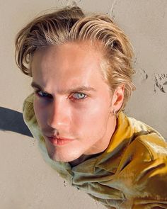 a man with blonde hair and blue eyes wearing a yellow jacket looking at the camera