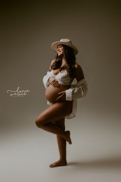 a pregnant woman wearing a white shirt and hat poses for the camera with her hands on her hips