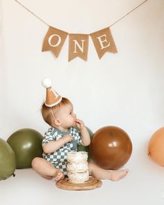 a baby sitting on the floor with a cake in front of him and balloons around him